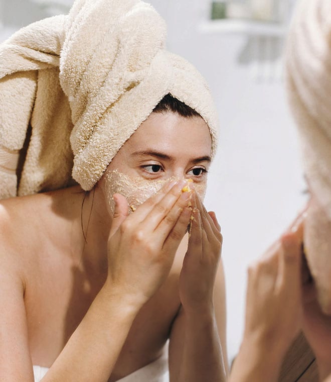 Young woman exfoliating her face in the mirror