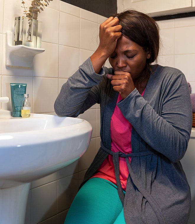 Black woman sitting in bathroom coughing into her hand