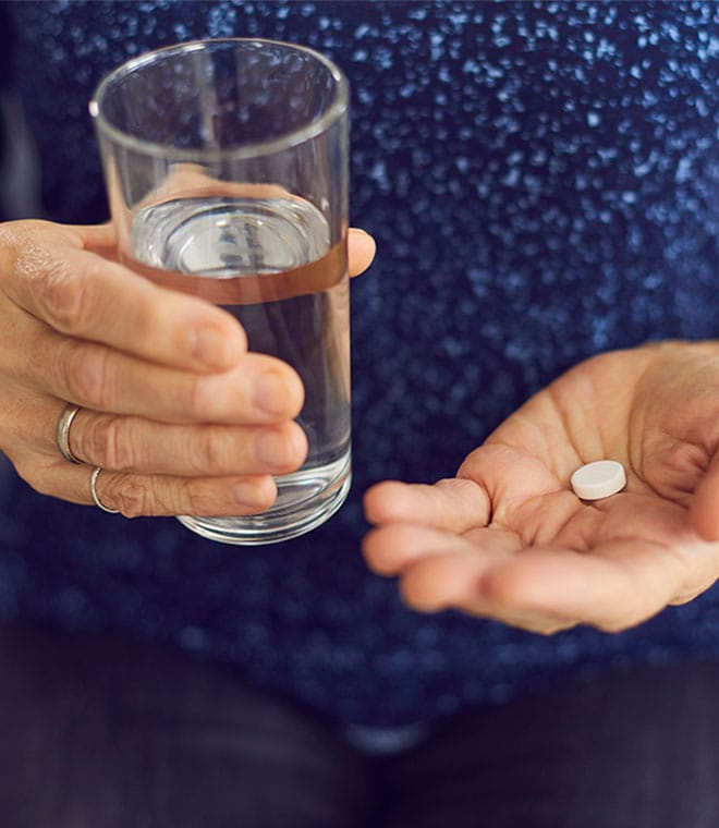 White man holding a glass of water and a pill