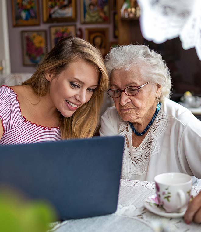 Young white woman helping older white woman use a laptop