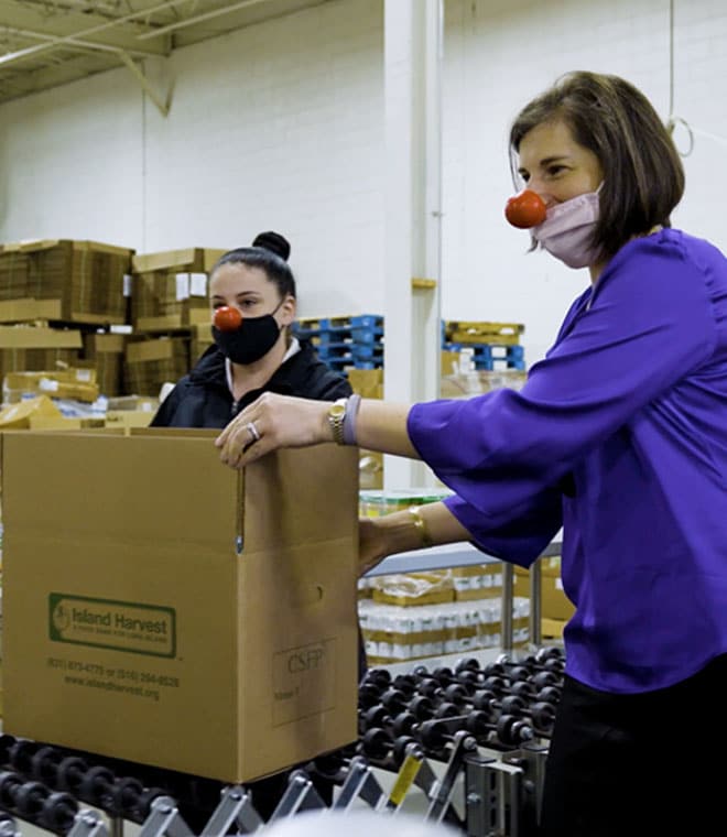 Two women wearing red noses processing boxed orders