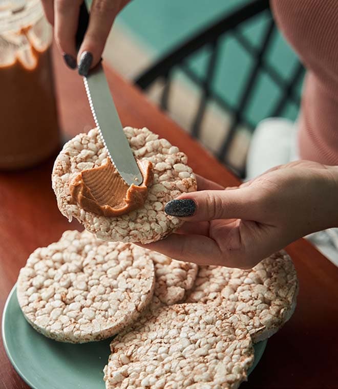 Person spreading peanut butter on a rice cake