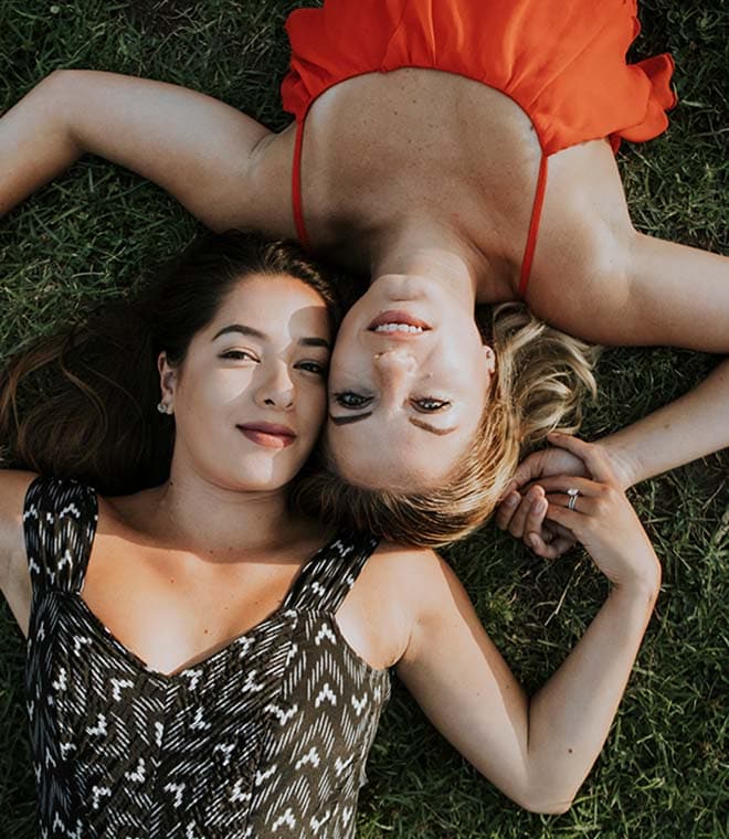 Two young women lying in the grass holding hands