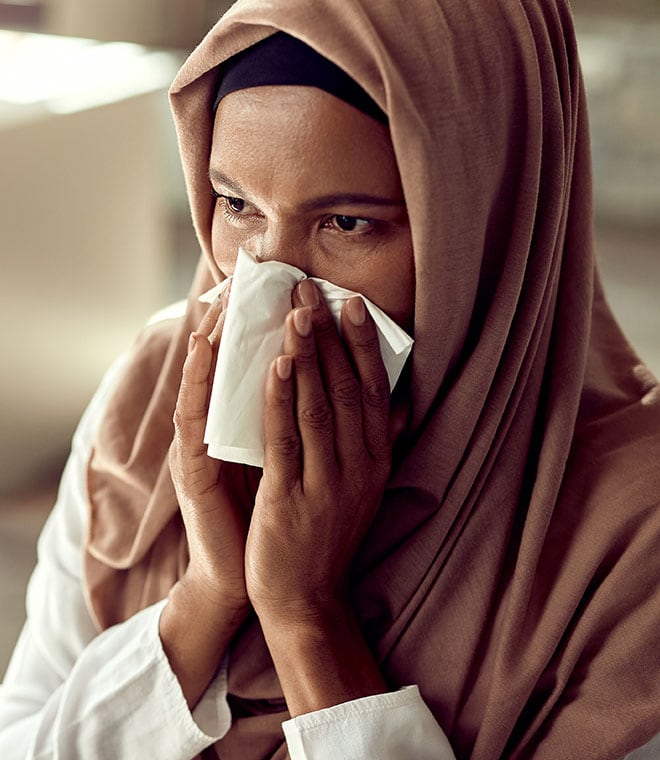 Middle aged woman in a hijab blowing her nose