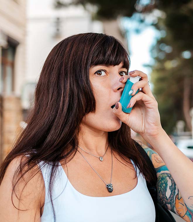 Millennial woman with tattoos using an inhaler