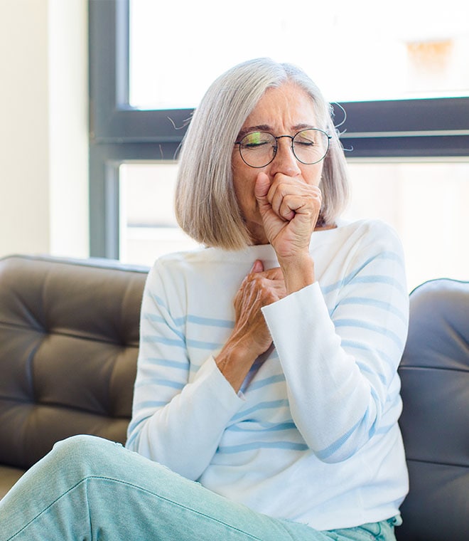 Older white woman covering her mouth while coughing