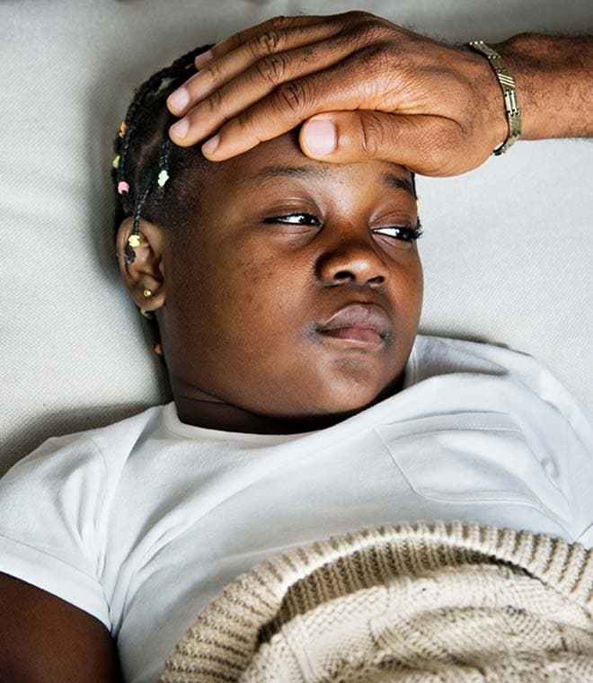 Caregiver checking young black child's forehead temperature