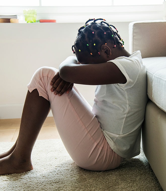 Young black girl sitting on the floor with her head down