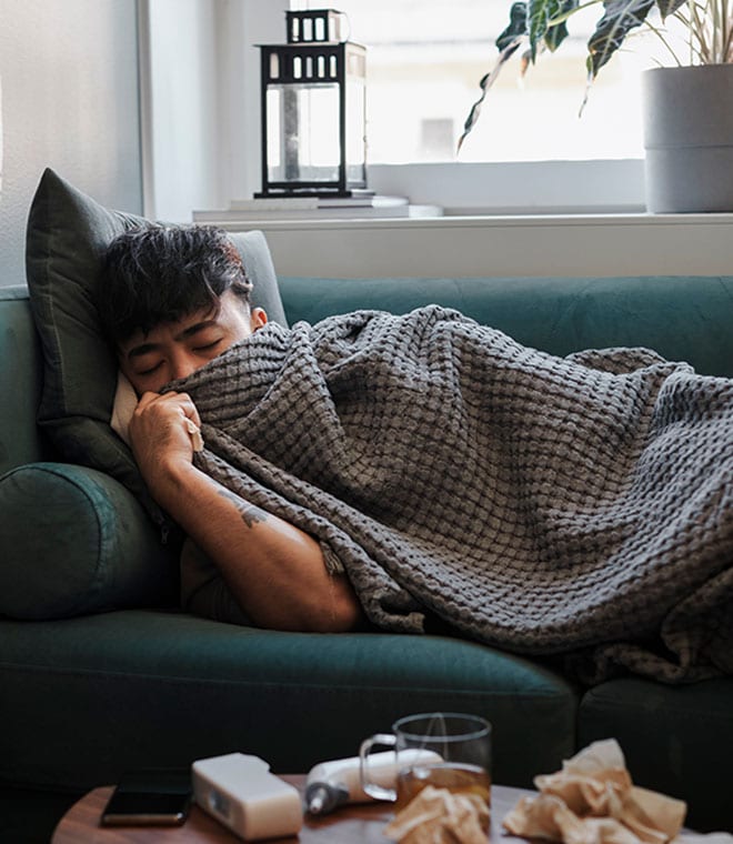 Young man laying on couch with a blanket