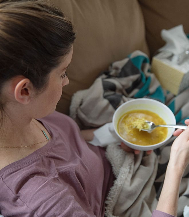White woman on couch eating soup