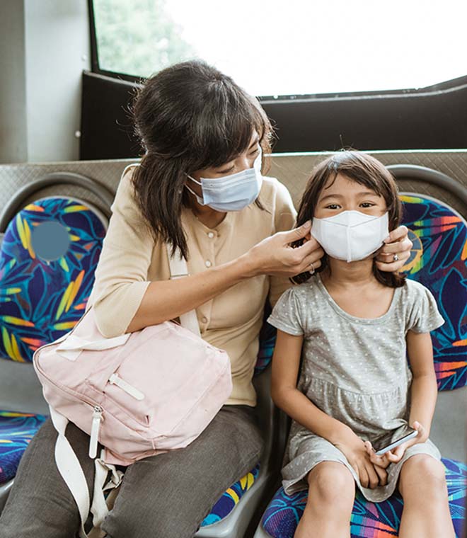 Asian woman adjusting face mask on young girl