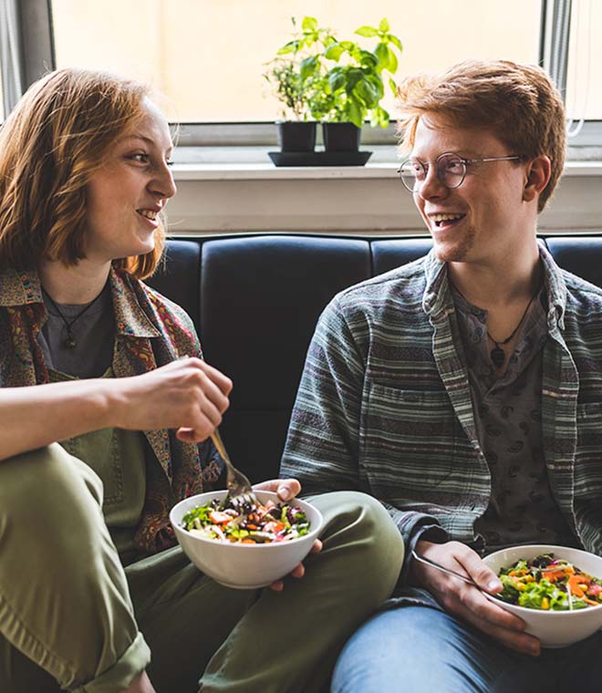 Two young adults laughing and eating salad