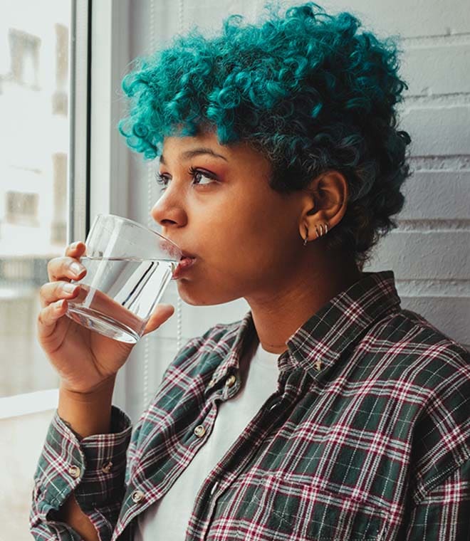 Young person with blue hair drinking water