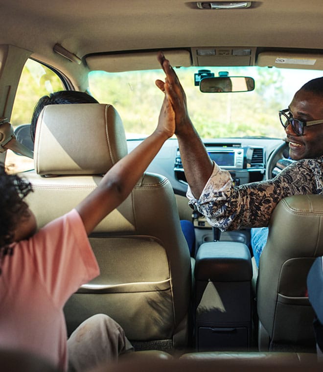 Black man in front seat of a car high fiving child in back seat