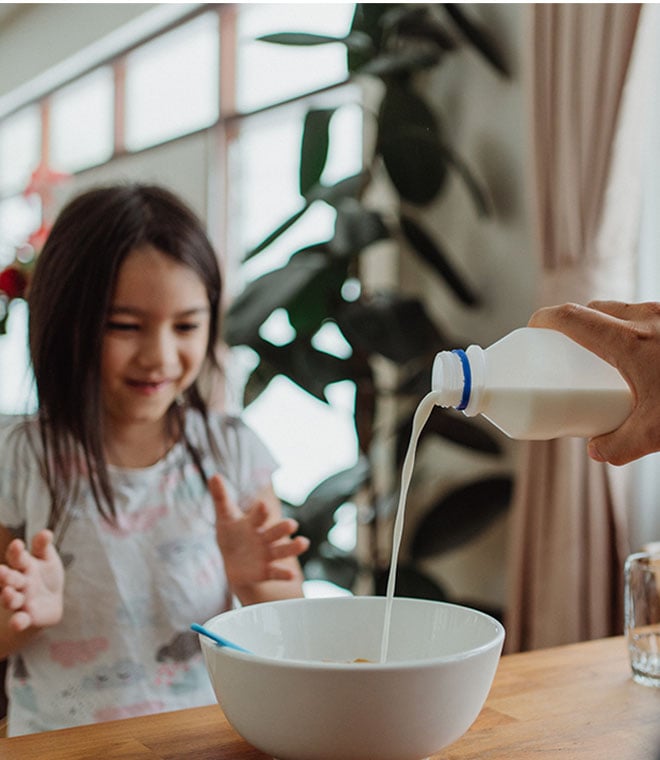 Girl watching milk being poured into cereal bowl