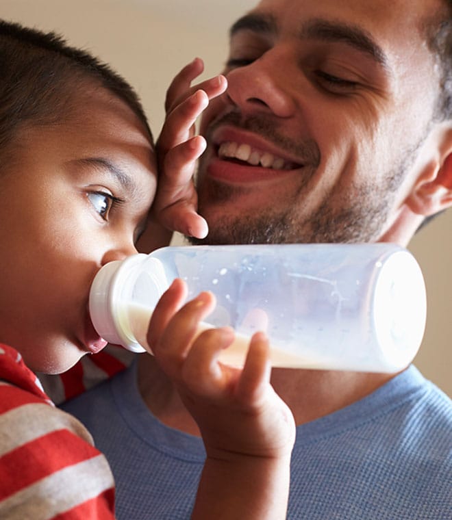 Father carrying young son drinking a bottle of milk