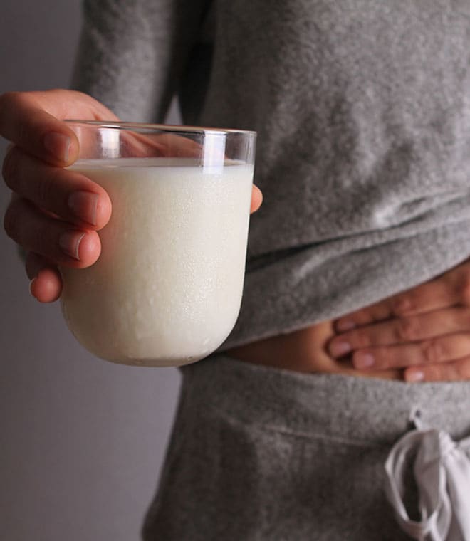Woman with stomach pain holding a glass of milk