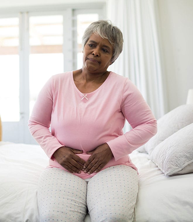 Older black woman sitting on the bed holding her stomach