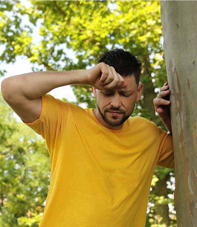 Spanish man leaning against a tree and holding his head