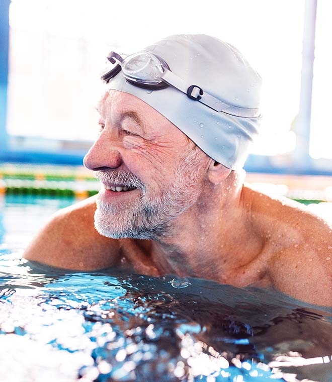 Older man in a pool with a swim cap and goggles