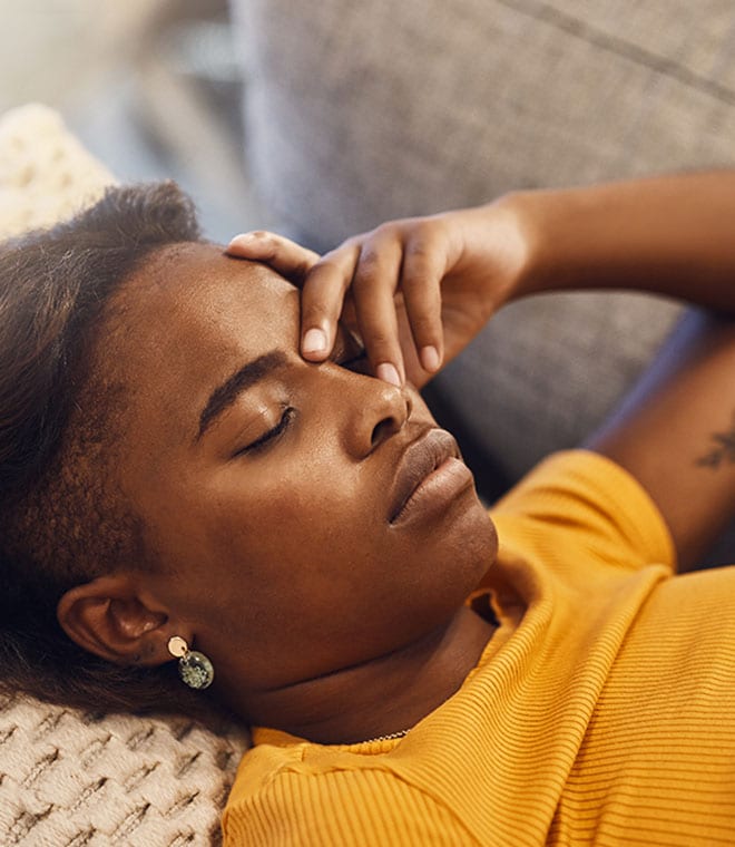 Black woman laying on couch holding her head