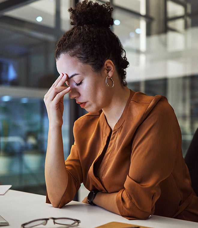 Woman with curly hair sitting at desk with headache