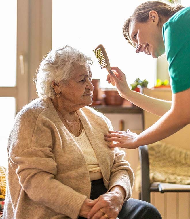Female nurse helping an elderly lady brush her hair