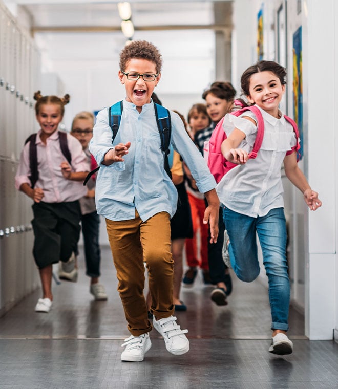 Several young children running through a school hallway