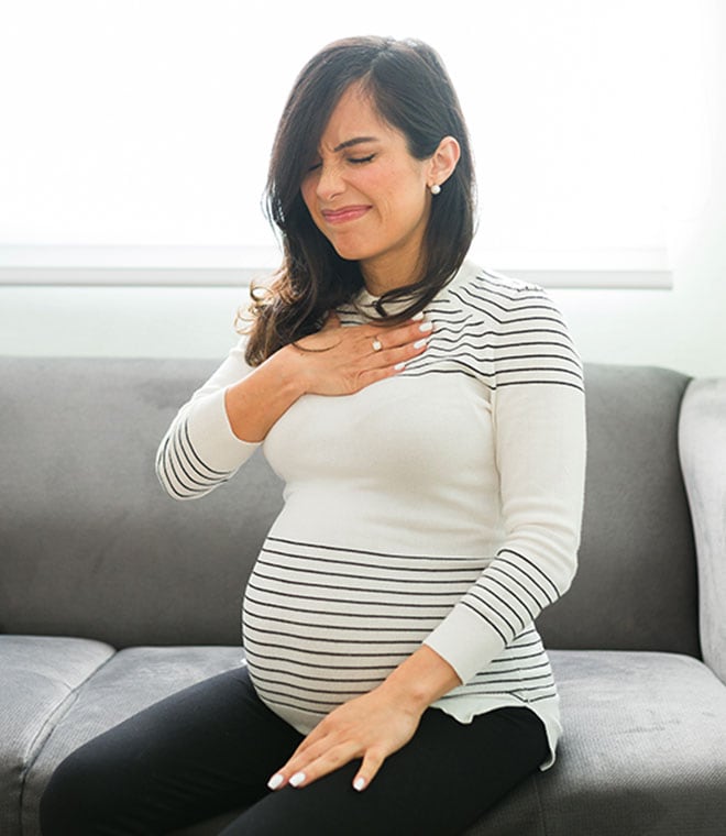 Pregnant woman on couch holding her chest