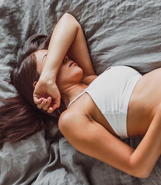 Pregnant woman laying on bed with arm over her head