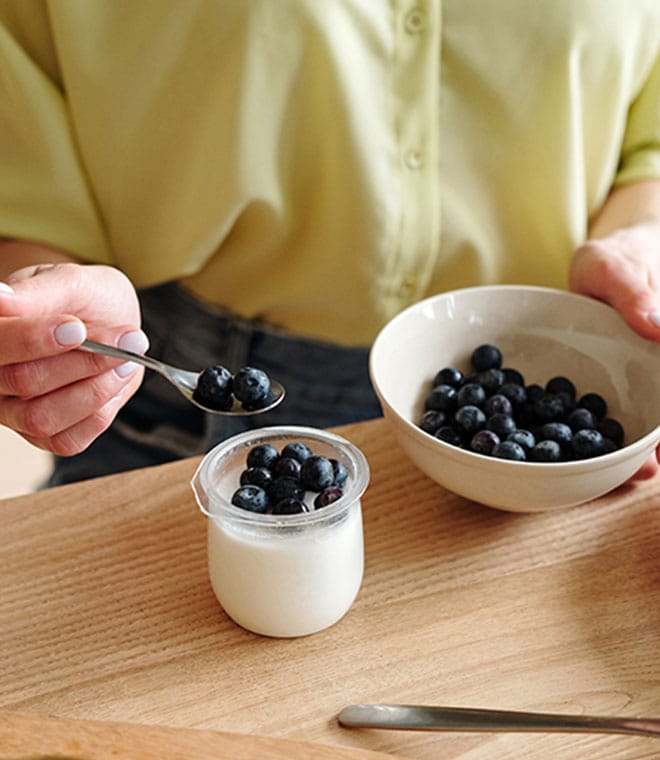 Woman spooning blueberries into a jar of yogurt
