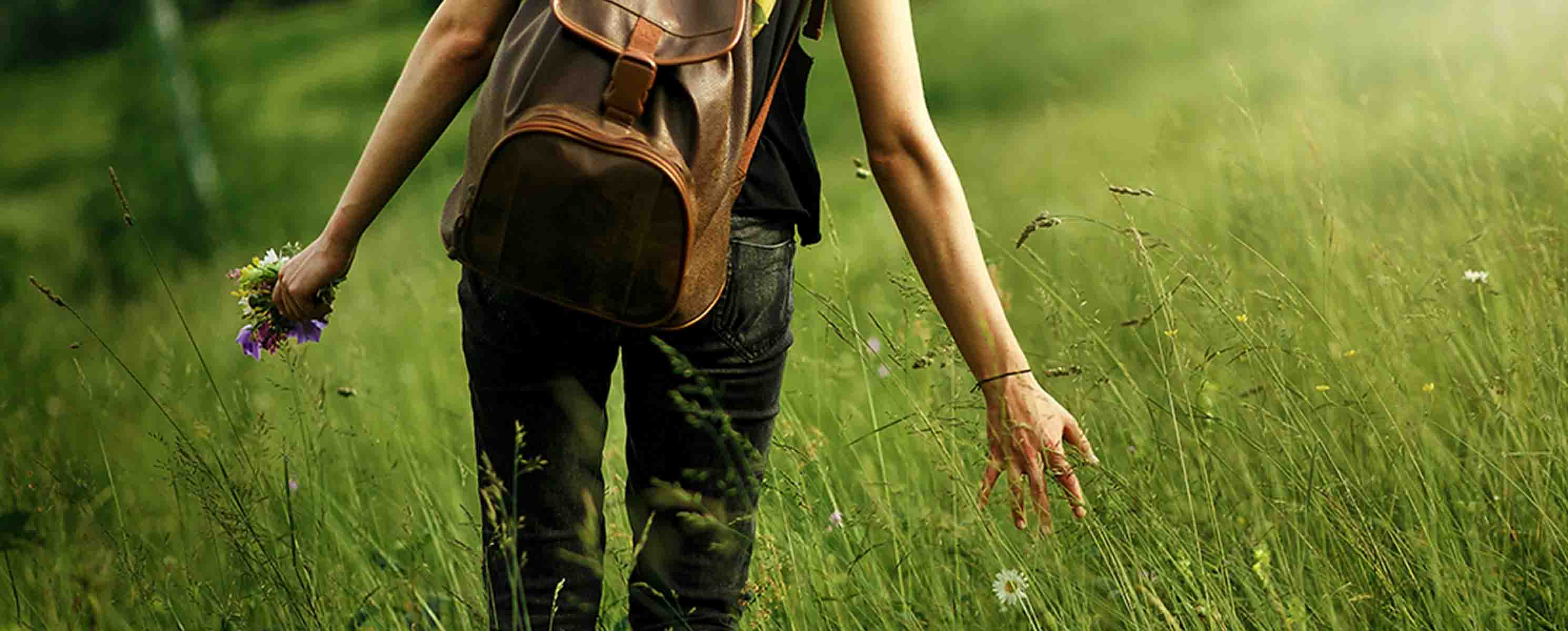 Woman walking through a field of long grass and wild flowers