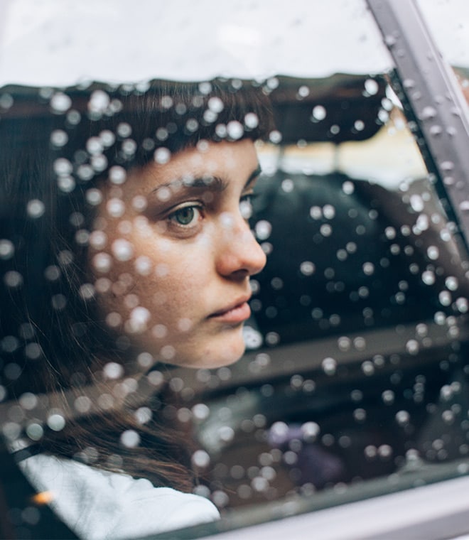 Young white woman sadly looking out rainy car window