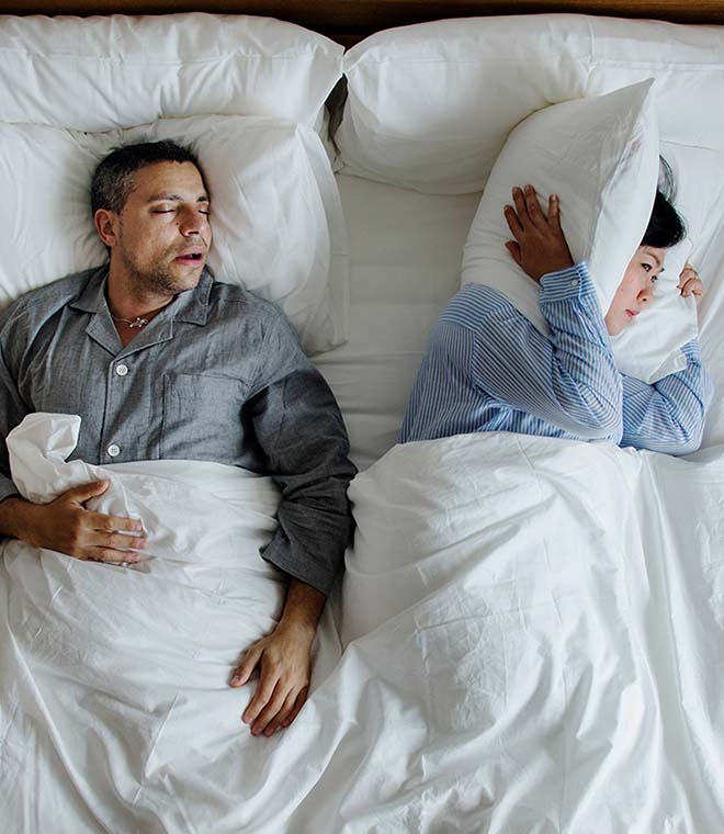 Man snoring and woman covering her ears with her pillow