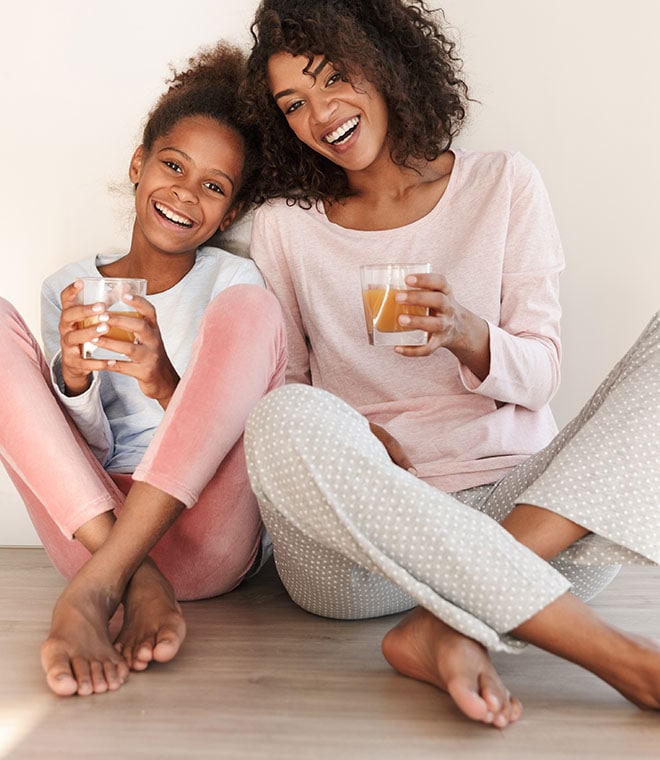 Young black mom and daughter smiling and drinking tea on the floor
