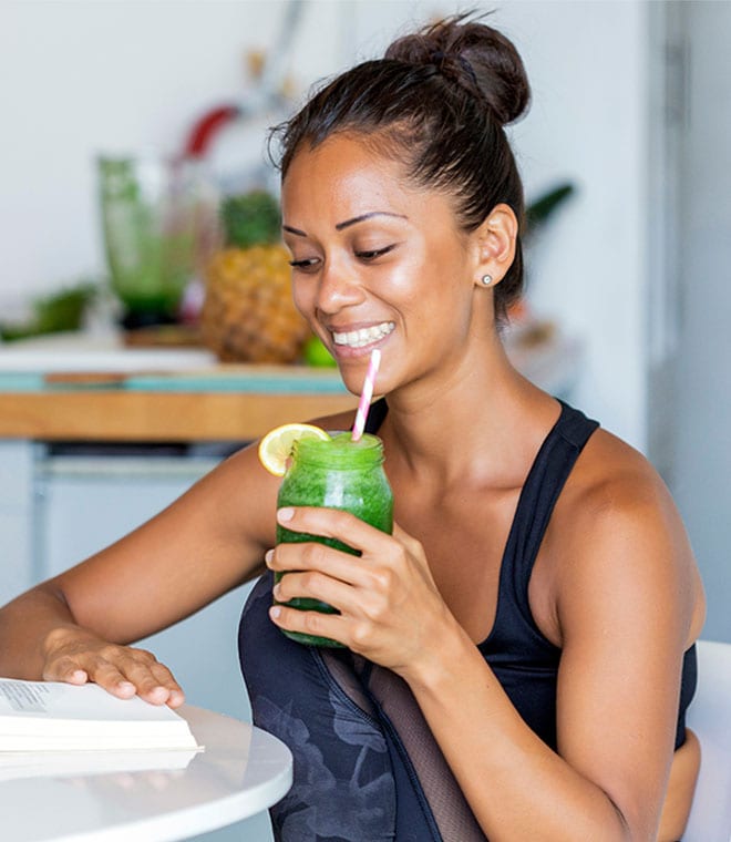 Young Latina woman drinking a green smoothie while reading