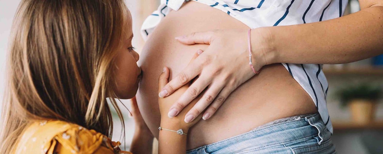 young blonde girl kissing her mother's pregnant belly