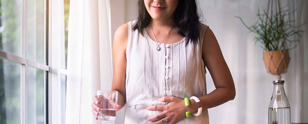 Woman standing by window holding her stomach and a glass of water