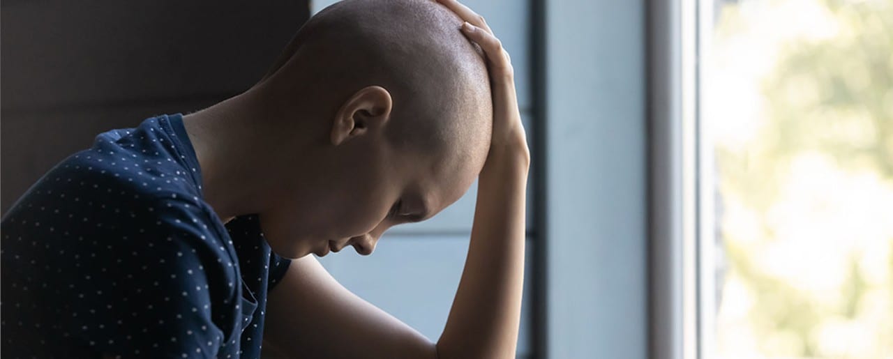 Woman with shaved head sitting on couch looking sad