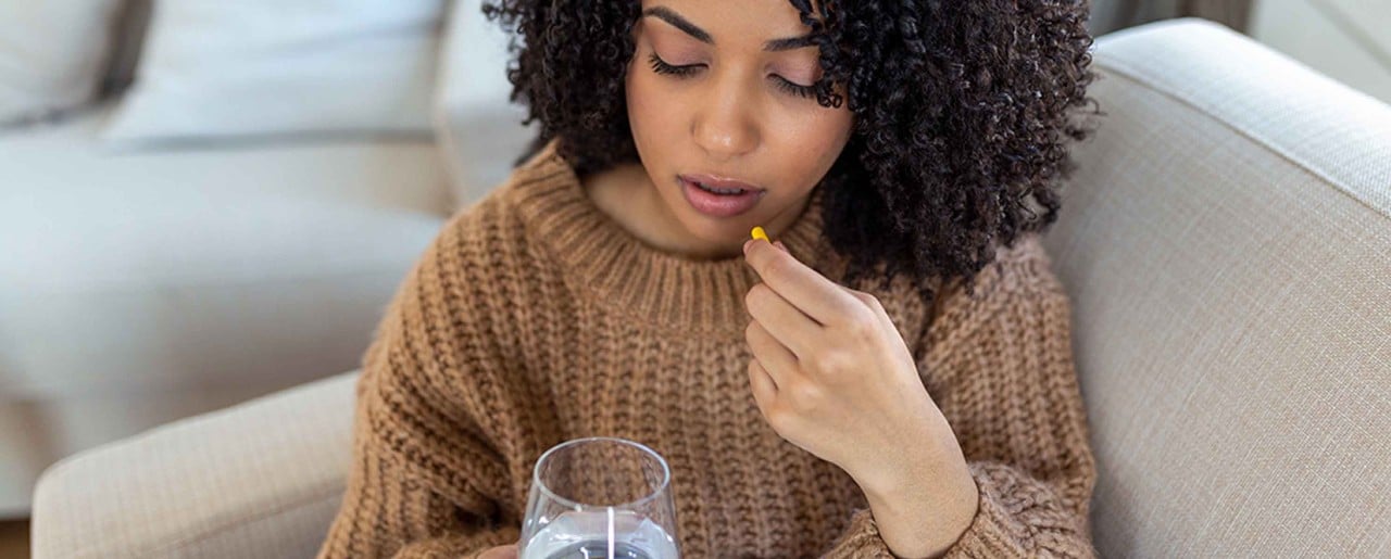 Black woman in brown sweater about to take a pill