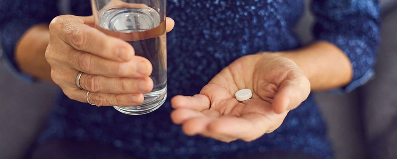 White man holding a glass of water and a pill