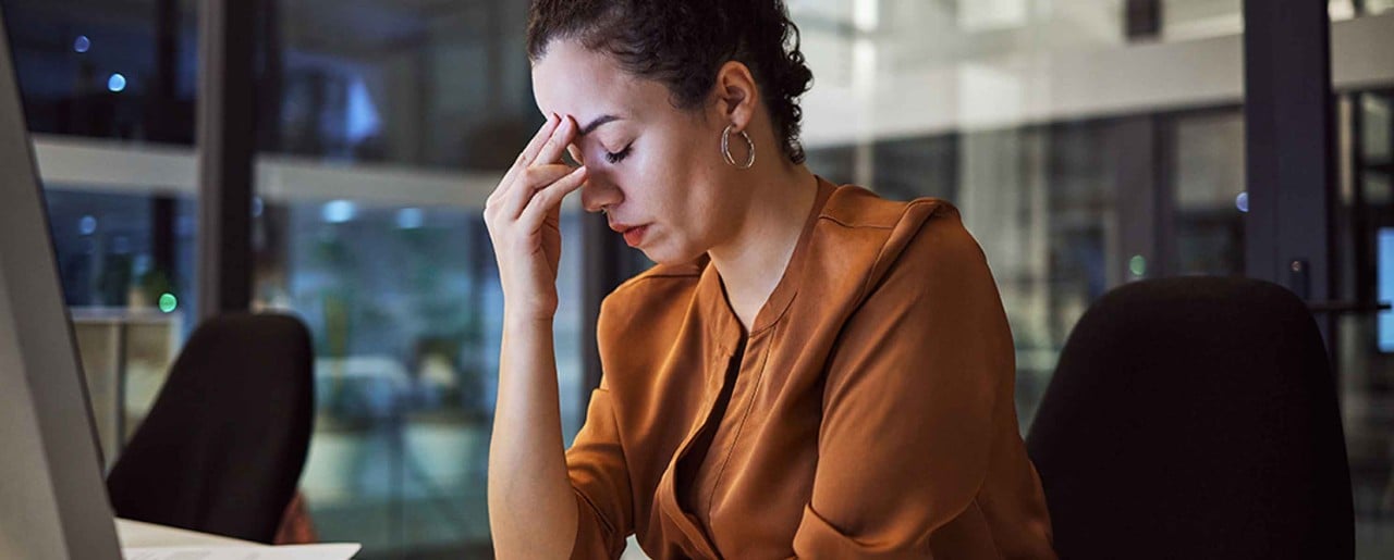 Woman with curly hair sitting at desk with headache
