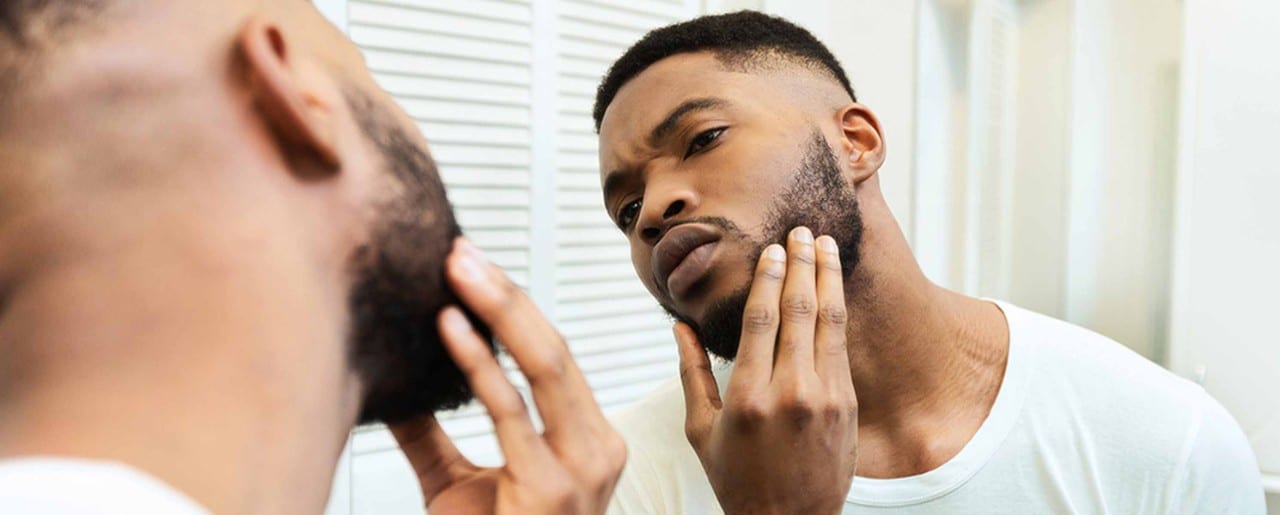 Young black man examining his face and beard