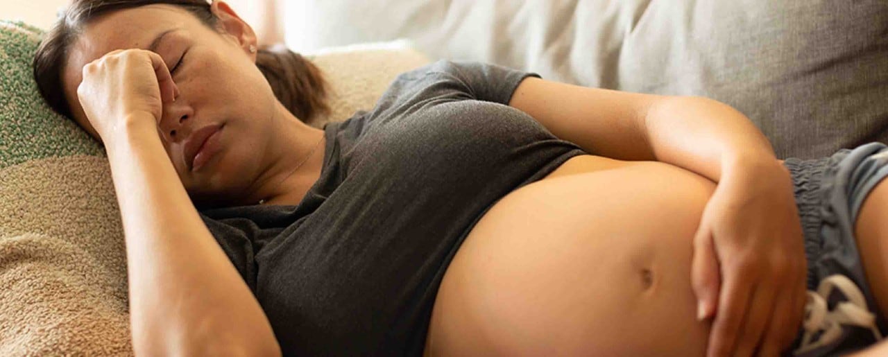 Pregnant woman laying on the couch holding her sinus