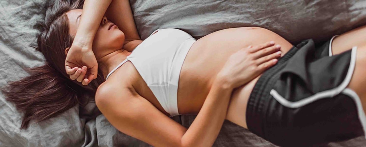 Pregnant woman laying on bed with arm over her head
