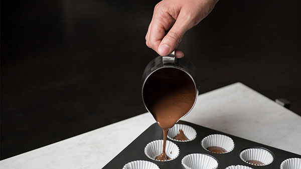 Photo of Pouring chocolate into small cups in a tray