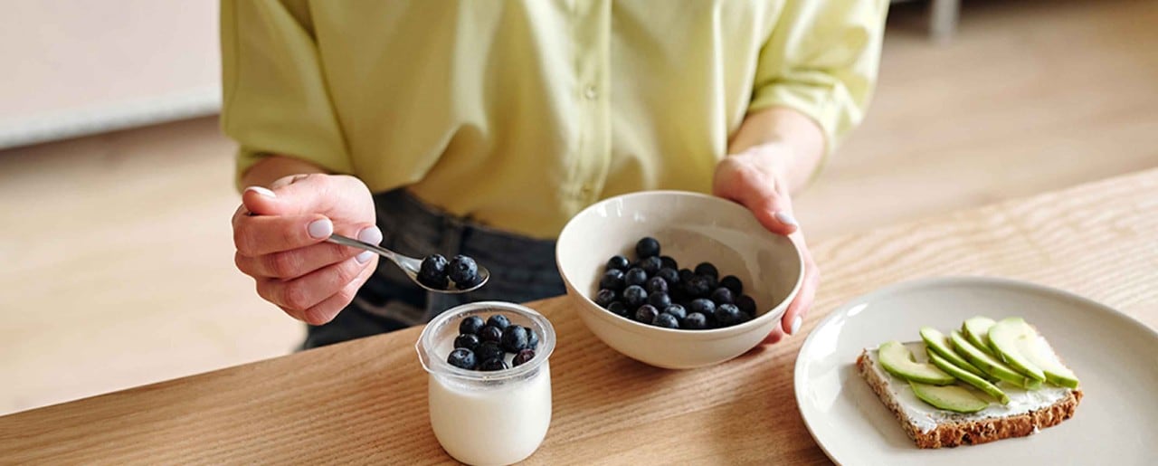 Woman spooning blueberries into a jar of yogurt