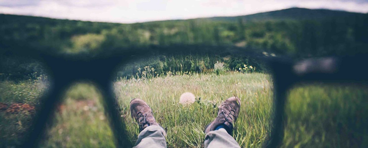 Man laying in a field through lens of glasses